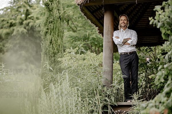 Businessman in a white shirt stands on the wooden jetty in the greenery,