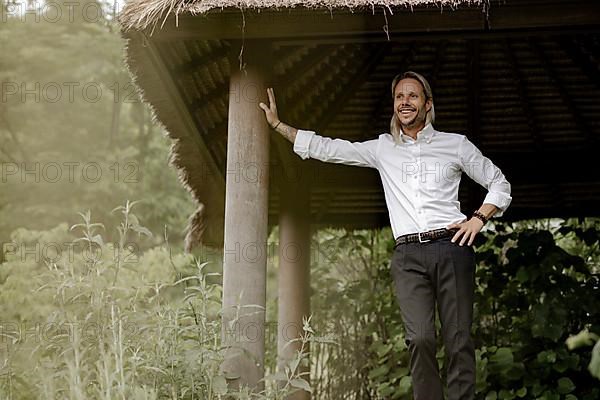 Businessman in a white shirt stands on the wooden jetty in the greenery,