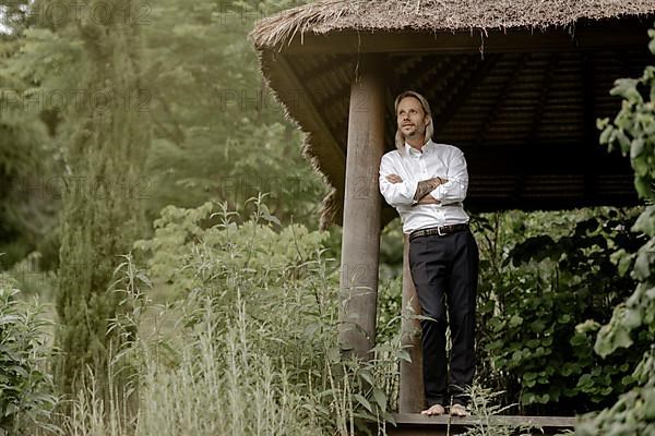 Businessman in a white shirt stands on the wooden jetty in the greenery,