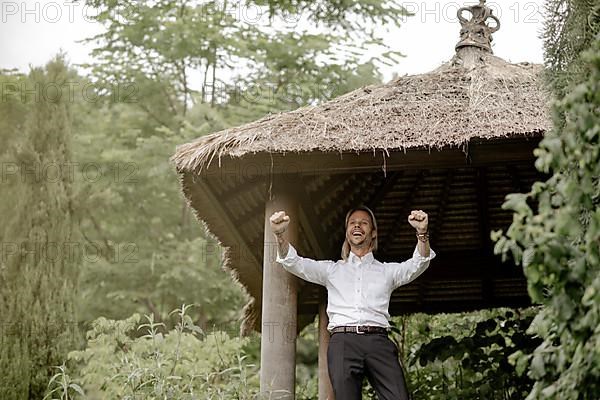 Businessman in a white shirt stands on the wooden jetty in the greenery,