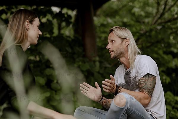 Tattooed man in conversation with woman in greenery,