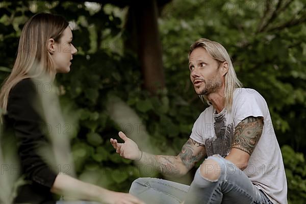 Tattooed man in conversation with woman in greenery,