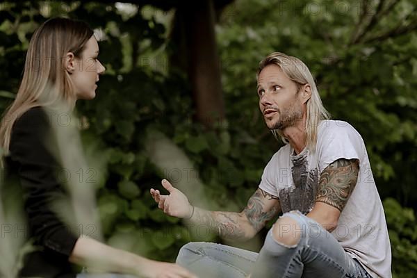 Tattooed man in conversation with woman in greenery,