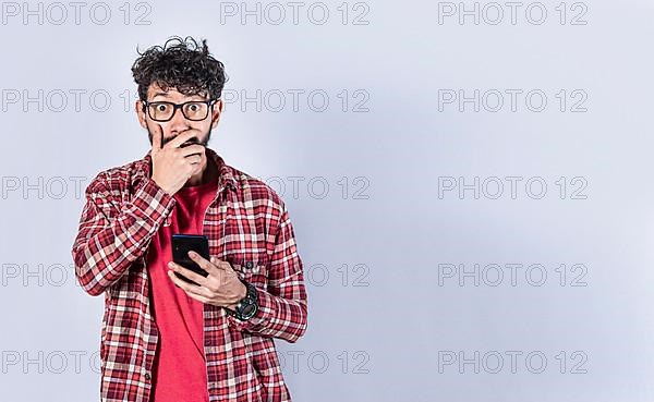 Man holding his cell phone and covering his mouth. surprised man receiving news on his cell phone isolated. Astonished man holding his cellphone and covering his mouth isolated,