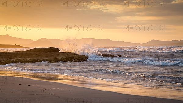 Sunset and breaking waves at the sandy beach playa in Son Serra de Marina, Tramuntana Mountains in the back