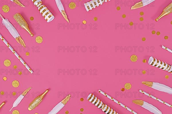 Party flat lay with golden and white decoration like confetti and feathers forming border around pink background,