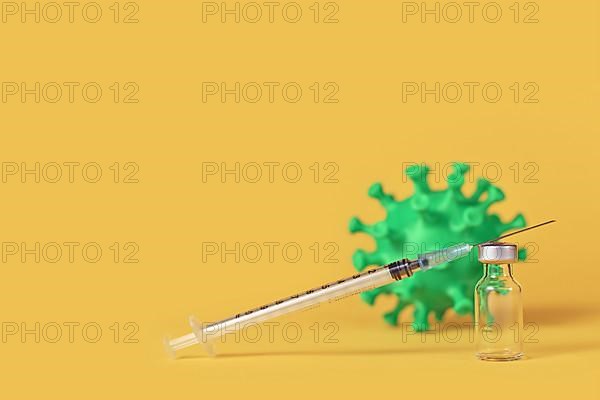 Corona vaccine vial with syringe and virus model in background on yellow background with copy space,