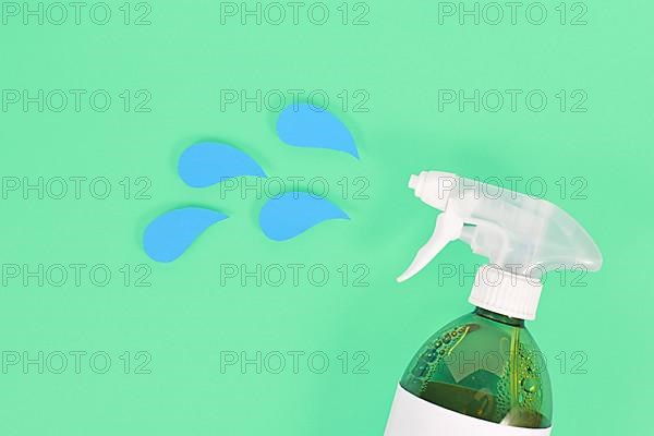 Green cleaning agent spray bottle with blue liquid drops cut from paper,