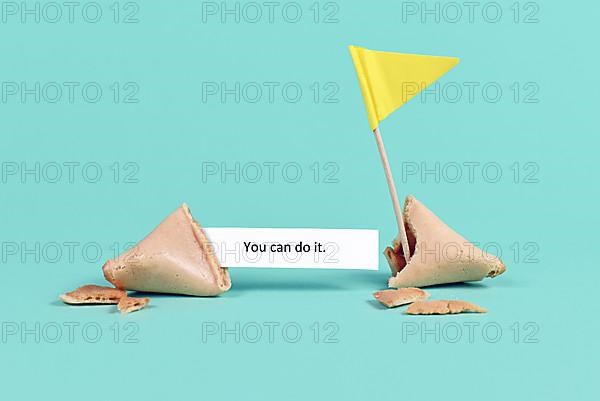 Fortune cookie with motivational text saying 'You can do it' with flag on real blue background,