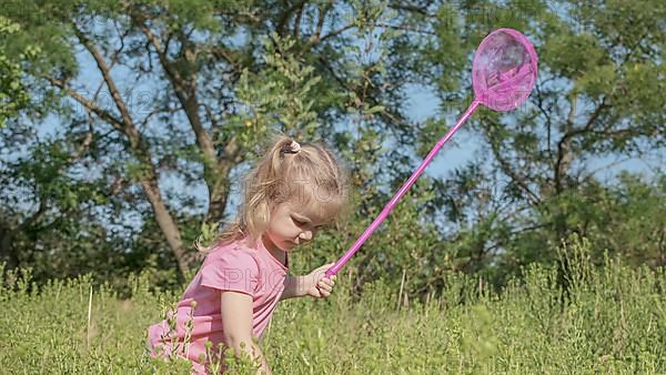 Little girl plays with butterfly net of tall grass in city park. Cute little girl is playing with aerial insect net in meadow on sun day. Odessa, Ukraine