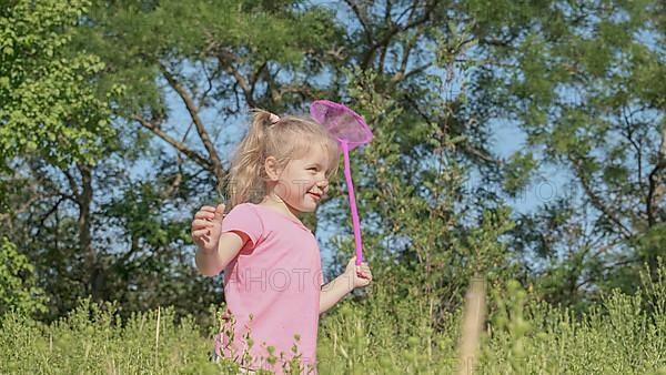 Little girl plays with butterfly net of tall grass in city park. Cute little girl is playing with aerial insect net in meadow on sun day. Odessa, Ukraine