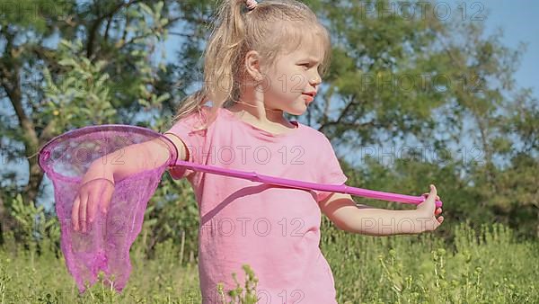 Little girl plays with butterfly net of tall grass in city park. Cute little girl is playing with aerial insect net in meadow on sun day. Odessa, Ukraine