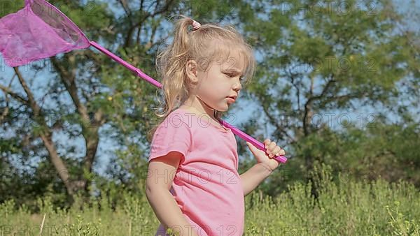 Little girl plays with butterfly net of tall grass in city park. Cute little girl is playing with aerial insect net in meadow on sun day. Odessa, Ukraine