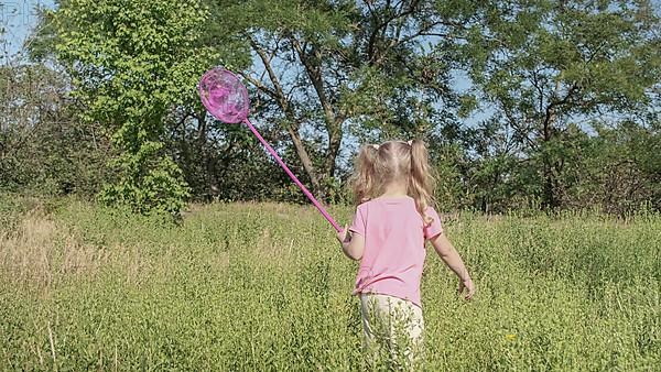 Little girl plays with butterfly net of tall grass in city park. Cute little girl is playing with aerial insect net in meadow on sun day. Odessa, Ukraine