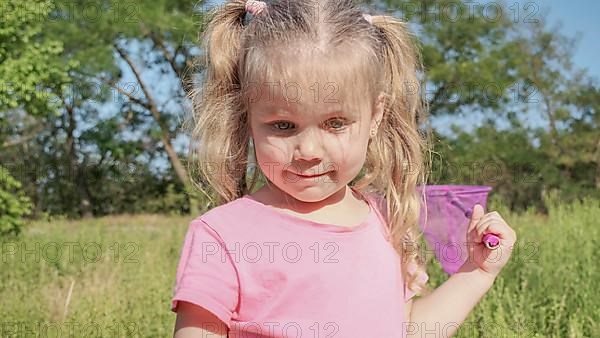 Little girl plays with butterfly net of tall grass in city park. Cute little girl is playing with aerial insect net in meadow on sun day. Odessa, Ukraine