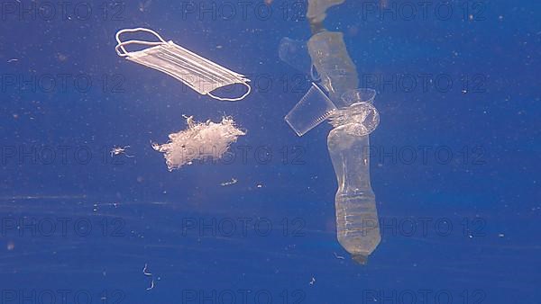Plastic bottle, cups and medical face mask swim in the blue water. Discarded plastic and other debris slowly drifting under surface of blue water in sunlight. Plastic pollution of the Ocean. Red sea