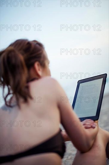 Woman on beach in bikini reading on tablet computer,