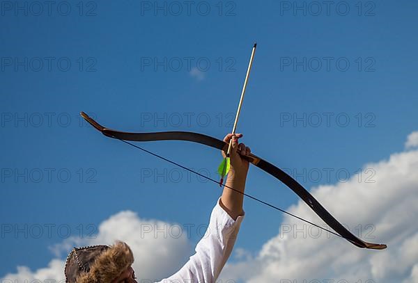 Archer with bow in traditional clothes shooting an arrow,
