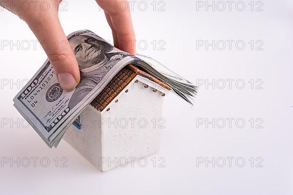 Hand holding American dollar banknotes on the roof of a model house on white background,