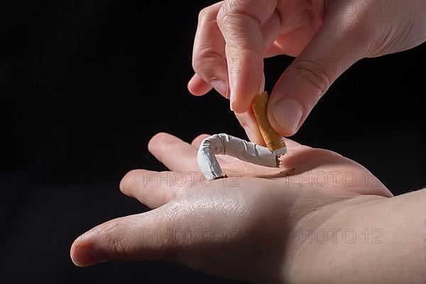 Hand is breaking a cigarette on a black background,