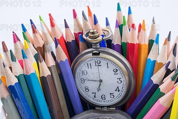 Retro style classic pocket watch and color pencils on white background,