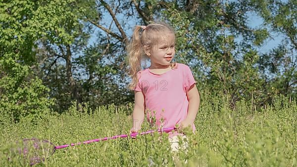 Little girl plays with butterfly net of tall grass in city park. Cute little girl is playing with aerial insect net in meadow on sun day. Odessa, Ukraine