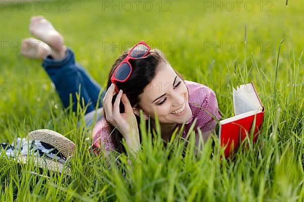 Young woman lying in meadow and reading a book,