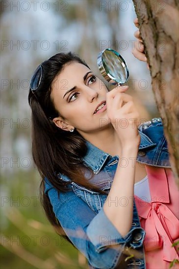 Woman looks at tree trunk under the magnifying glass,