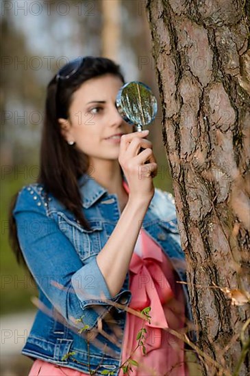 Woman looks at tree trunk under the magnifying glass,