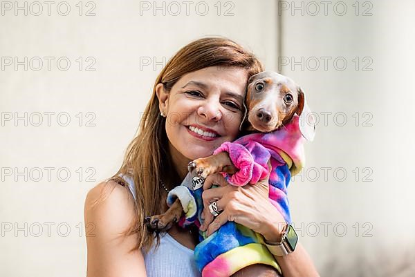 Latin woman holding her dog. Both are dressed alike and looking at camera,