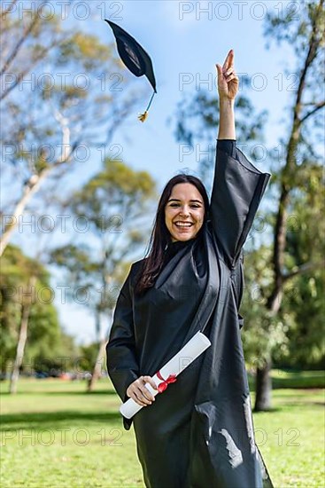 Happy caucasian graduated girl in a black gown throwing the mortarboard to the sky,