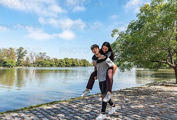 Happy couple. Handsome young man carrying his beautiful girlfriend on his back. They are looking at camera,