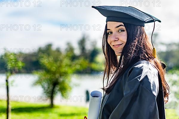 Happy caucasian graduated girl with long brown hair, holding a diploma and looking at camera