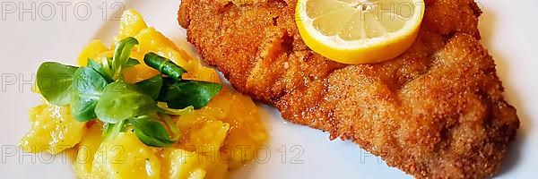 Delicious golden-brown fried Wiener Schnitzel with potato salad and a slice of lemon on a white plate,