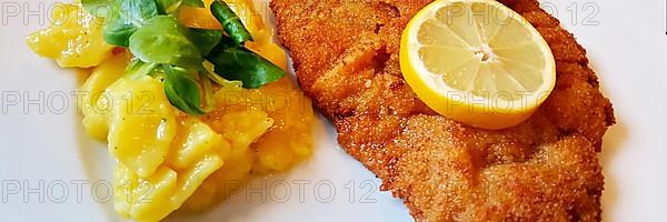 Delicious golden-brown fried Wiener Schnitzel with potato salad and a slice of lemon on a white plate,