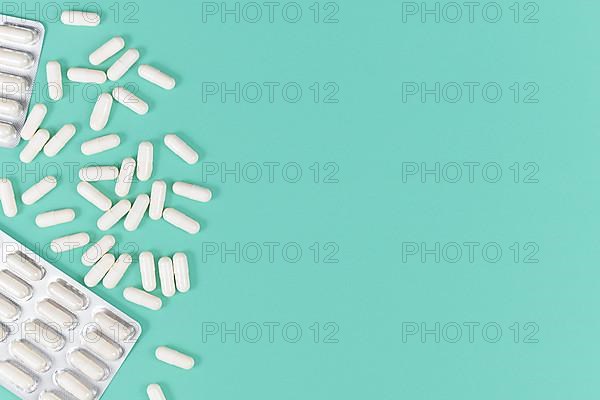 White capsule pills on left side of mint green background with blank copy space,