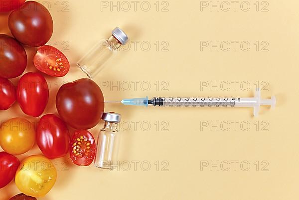 Concept for genetically modified food with tomatoes, injected syringe and empty medical vials on yellow background