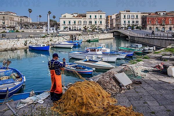 Fishermen mending nets at the fishing harbour with boats in front of the old town, Syracuse