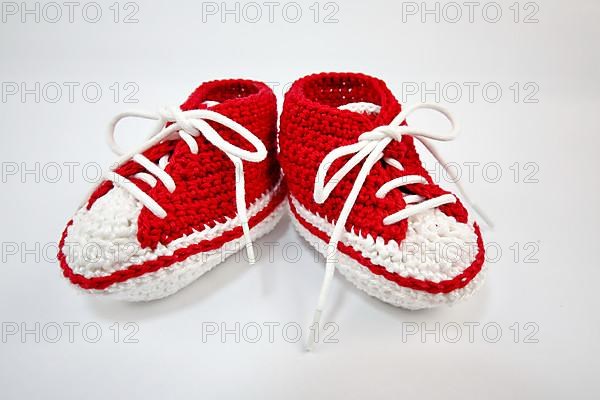 Baby shoes or crochet shoes in red and white isolated against a white background,