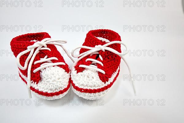 Baby shoes or crochet shoes in red and white isolated against a white background,