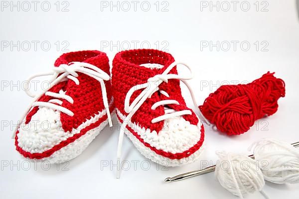 Baby shoes or crochet shoes in red and white isolated against a white background,