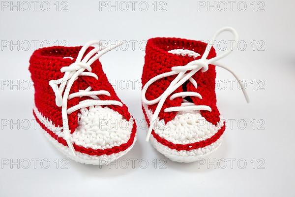 Baby shoes or crochet shoes in red and white isolated against a white background,