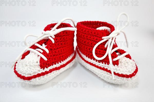 Baby shoes or crochet shoes in red and white isolated against a white background,