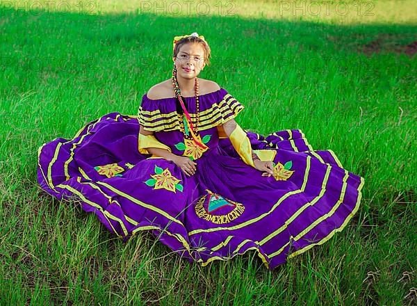 Young Nicaraguan woman in traditional folk costume sitting on the grass in the field, Portrait of Nicaraguan woman in folk costume sitting on the grass