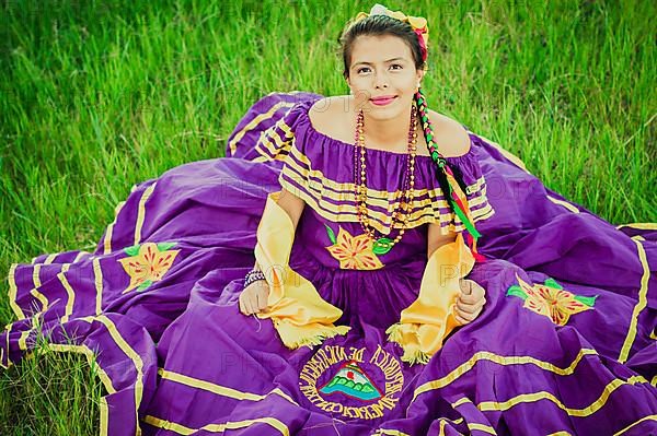 Portrait of Nicaraguan woman in folk costume sitting on the grass, Young Nicaraguan woman in traditional folk costume sitting on the grass in the field