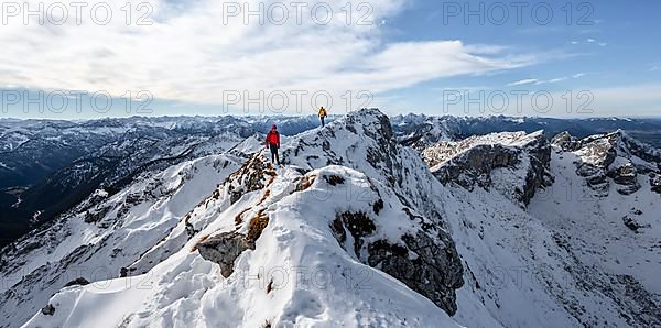 Two mountaineers on a narrow rocky snowy ridge, behind peak crow