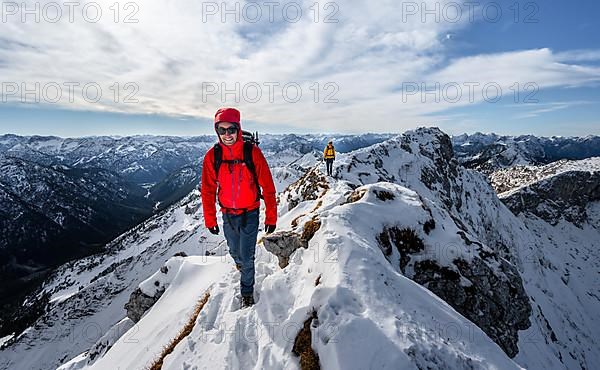 Two mountaineers on a narrow rocky snowy ridge, behind peak crow