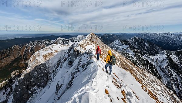 Two mountaineers on a narrow rocky snowy ridge, in the back summit of the Ammergauer Hochplatte with summit cross