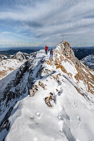 Two mountaineers on a narrow rocky snowy ridge, in the back summit of the Ammergauer Hochplatte with summit cross