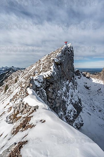 Mountaineer stretching his arms in the air, standing on a snow-covered rocky ridge